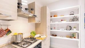 A modern kitchen with a gas stove, wooden cabinets, and a white shelving unit with kitchenware.