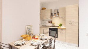 A modern kitchen with light wood cabinets, a dining table set for two, and a small island with a basket.