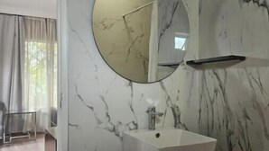 A bathroom with a marble wall, a round mirror, a white sink, and a red trash bin.