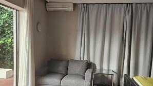 A room with a grey sofa, a small table, and a bed with a yellow bedspread.