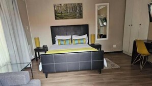 A bedroom with a bed, bedside tables, a chair, a couch, and a painting on the wall.