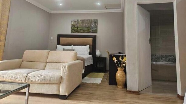 Un dormitorio moderno con una cama, un sofá, una mesita de noche y un jarrón con flores.