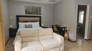 Un dormitorio con cama, sofá, escritorio y un cuadro en la pared.