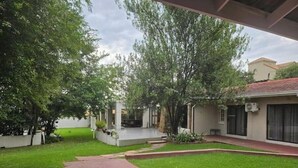 Un patio con suelo de ladrillo rojo, césped verde y árboles.