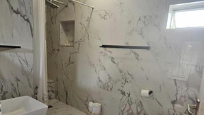 Un baño con paredes de mármol, una bañera, un inodoro y una zona de ducha.