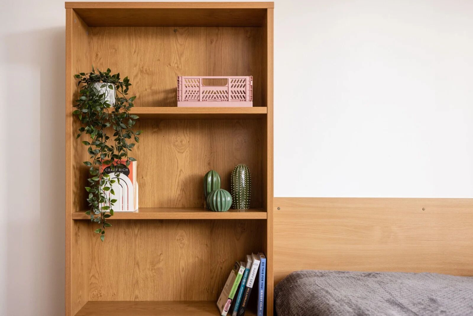 A wooden bookshelf with a plant, a pink crate, and two green vases.