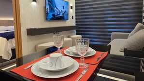 A modern hotel room with a dining area, a TV mounted on the wall, and a window with blinds. - Flat vip 02C Bela Vista by La Playa (Ipojuca)