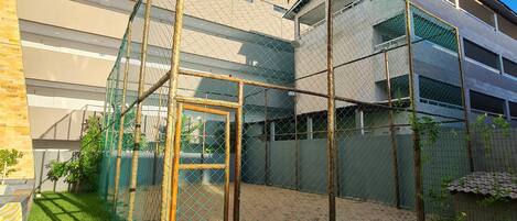 A fenced outdoor area with artificial grass, a wooden structure, and a building in the background.