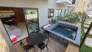 A modern outdoor patio with a black table and chairs, a small hot tub, and a glass door leading to an indoor area with a dining table and chairs. - Flat vip 02C Bela Vista by La Playa (Ipojuca)