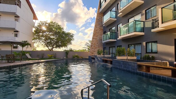 A swimming pool with a metal ladder, surrounded by buildings with balconies and outdoor seating. - Flat vip 02C Bela Vista by La Playa (Ipojuca)