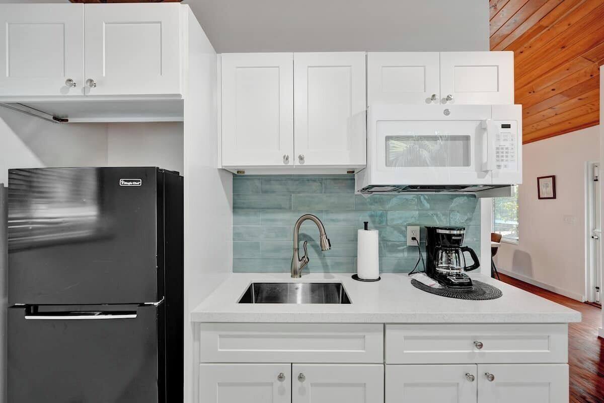 A kitchen with white cabinets, a black refrigerator, a white microwave, and a sink with a faucet.