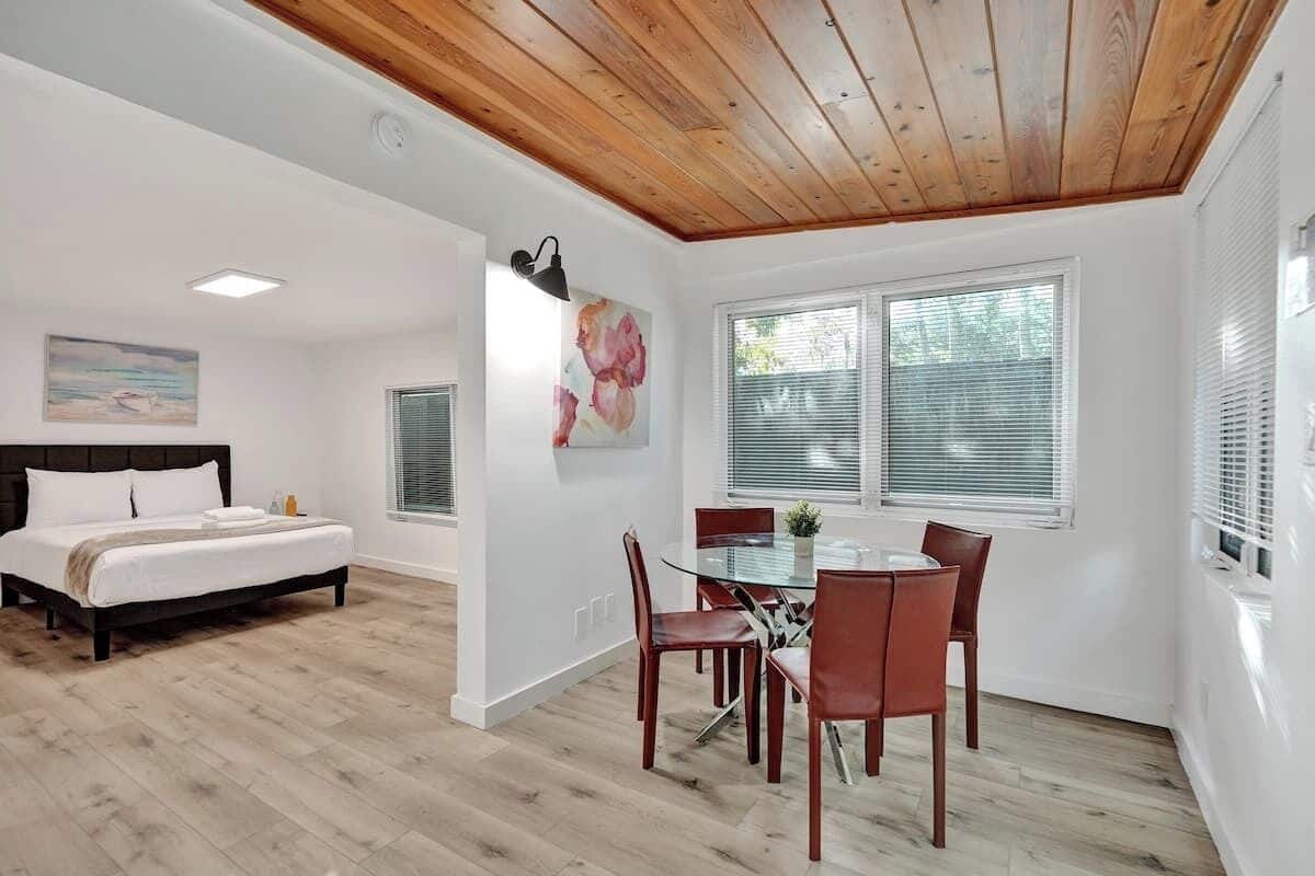 A modern bedroom with a wooden ceiling, a large bed, and a dining area with a glass table and chairs.