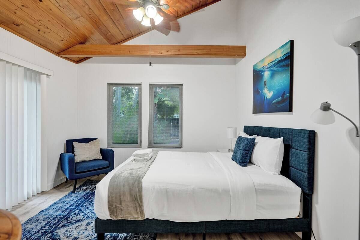 A bedroom with a bed, a chair, a painting, and a ceiling fan.