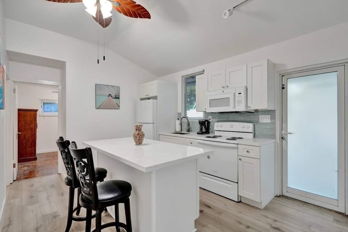 A modern kitchen with white cabinetry, a central island with bar stools, a microwave, and a stove.