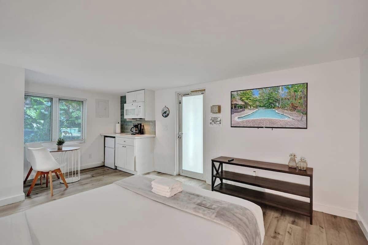 A bedroom with a bed, a desk, a chair, a small table, and a painting of a pool.