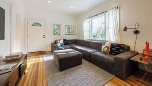 A modern living room with a sectional sofa, a small ottoman, a wooden coffee table, and a large window with curtains.