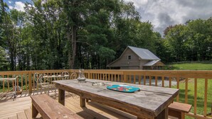 A wooden deck with a table and benches, surrounded by a fence and trees.