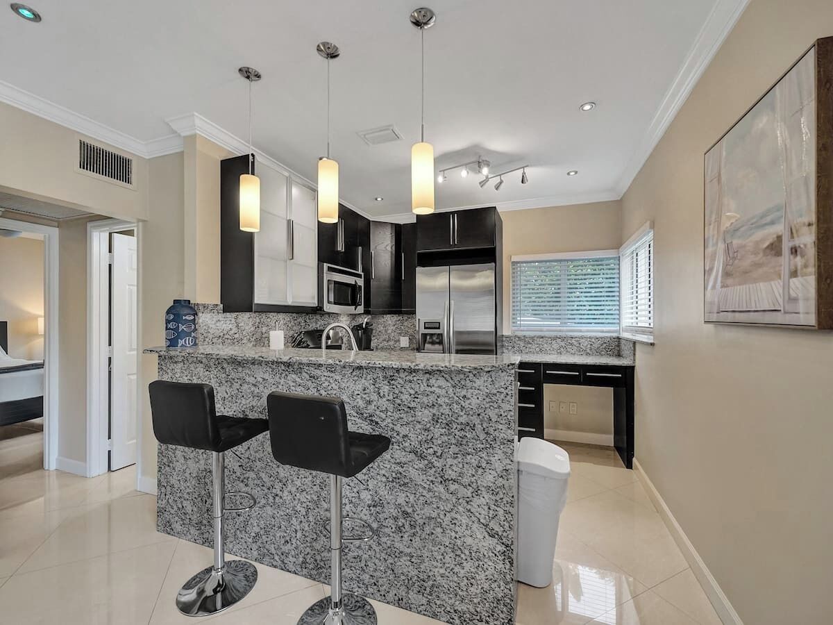 A modern kitchen with granite countertops, stainless steel appliances, and black bar stools.