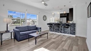 A modern living room with a sofa, coffee table, and a dining area with bar stools.