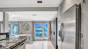 A modern kitchen with a stainless steel refrigerator, a marble countertop, and a dining area with a table and chairs.
