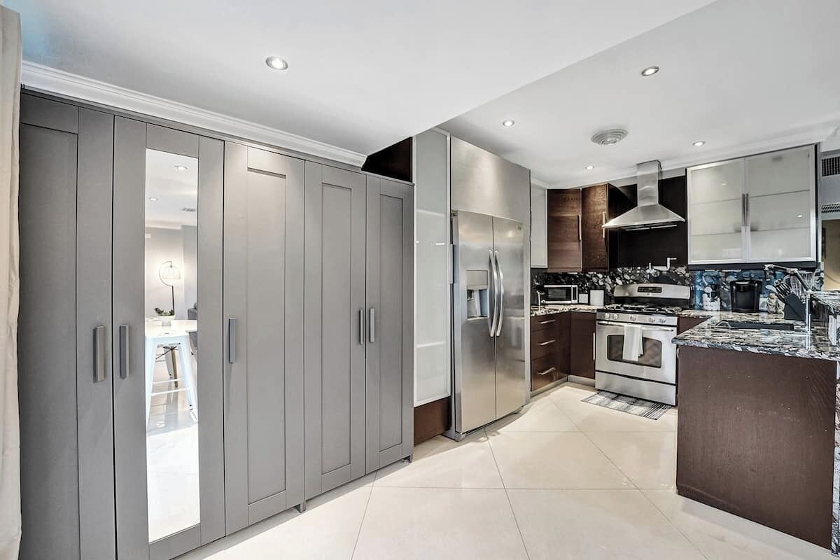 A modern kitchen with grey cabinets, stainless steel appliances, and a marble countertop.