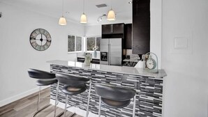 A modern kitchen with a central island, bar stools, pendant lighting, a clock, and a refrigerator.