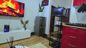 A modern kitchen with a flat-screen TV, a refrigerator, a microwave, and red cabinets. - Fefe's Mikocheni 1 BR Apartment (Dar es salaam)