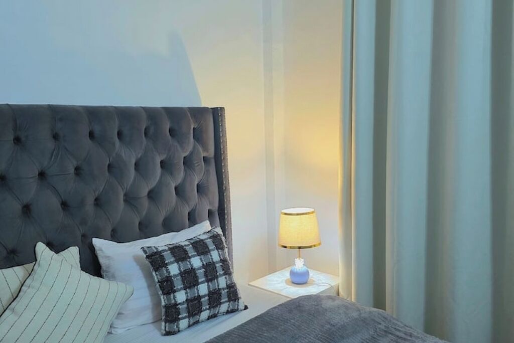 A neatly made bed with a tufted headboard, a bedside lamp, and a plaid pillow.
