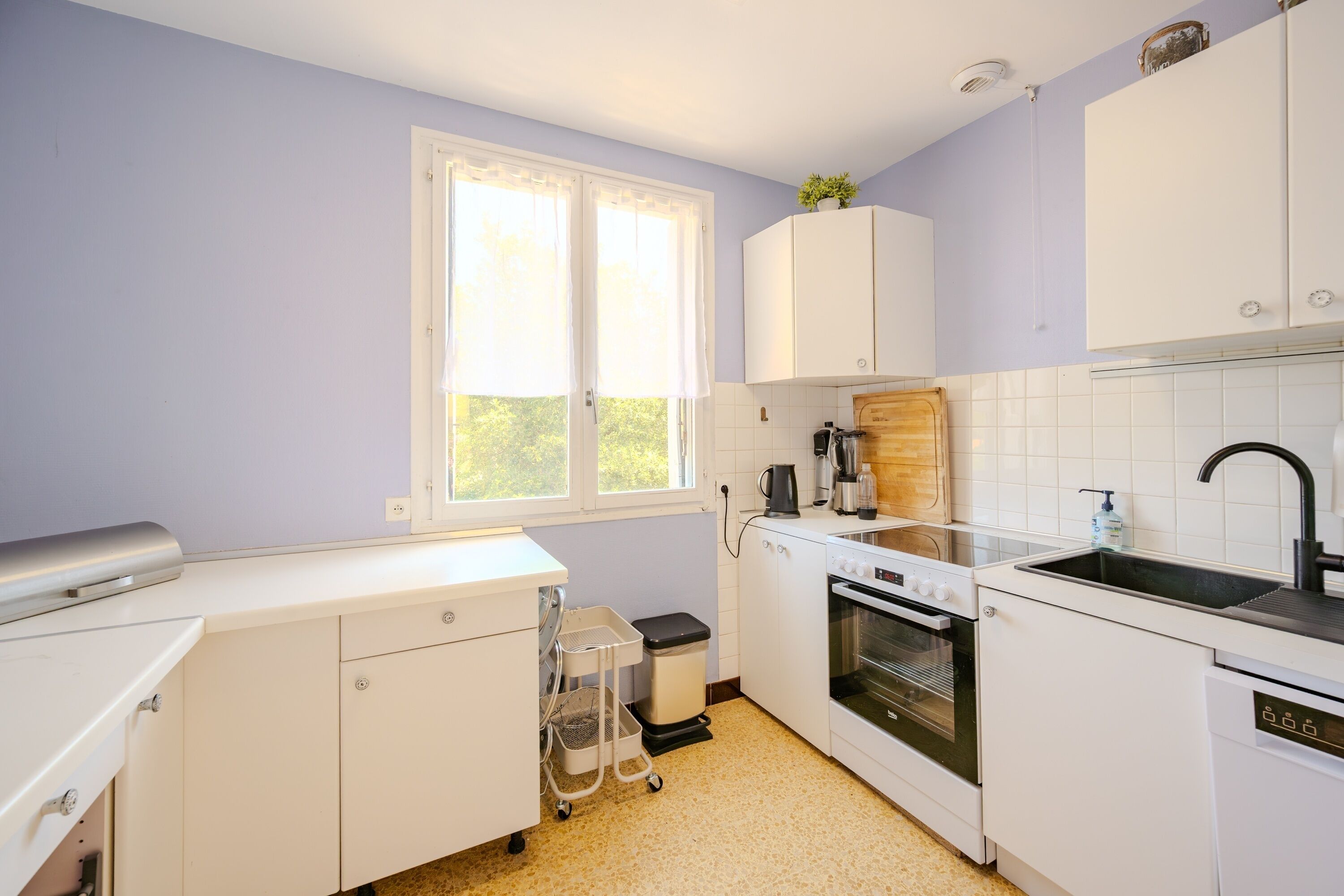 A kitchen with white cabinets, a sink, an oven, and a window with curtains.