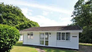 A small, single-story building with a white exterior and a dark roof, surrounded by lush greenery. - 4 Rosecraddoc Lodge Holiday Bungalows (Liskeard)