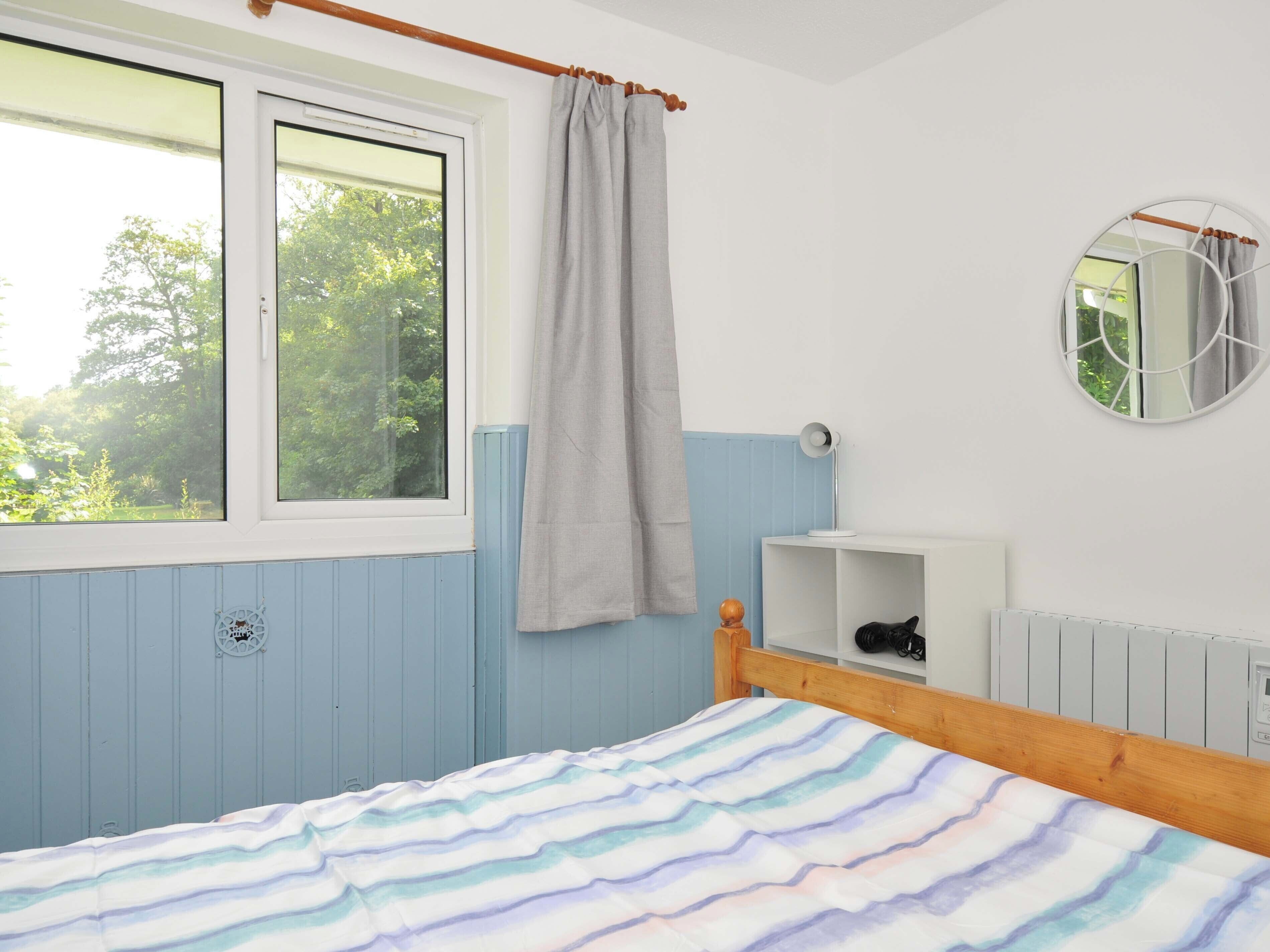 A bedroom with a bed, a window with curtains, a bedside table with a lamp, and a radiator.