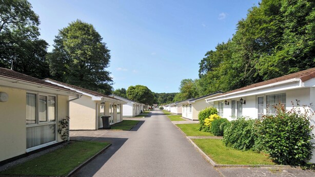 A row of mobile homes with a paved driveway, surrounded by greenery and trees. - 4 Rosecraddoc Lodge Holiday Bungalows (Liskeard)
