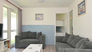 A living room with a grey sofa, a white coffee table, and a television on a stand. - 4 Rosecraddoc Lodge Holiday Bungalows (Liskeard)