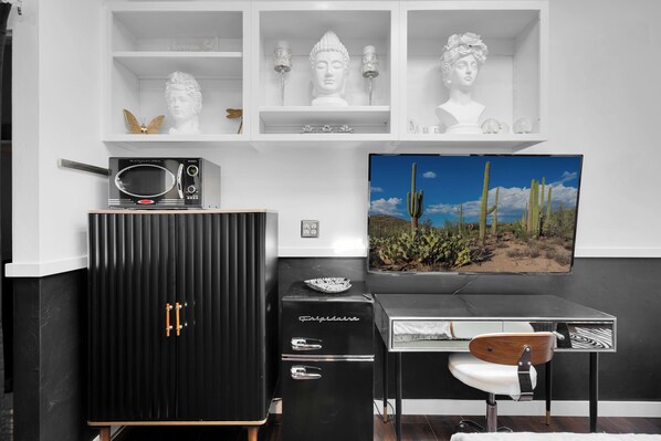 A modern room with a black cabinet, a vintage radio, a desk with a chair, and a large TV displaying a desert landscape. - West University Bungalow w/Private Studio! (Tucson)
