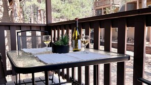 A wooden deck with a table and chairs, a bottle of wine, and a glass on the table. - JUST LISTED!!  REMODELED!!  Angel Fire 2B/2B Condo (Angel Fire)