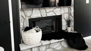 A living room with a stone fireplace, a flat-screen TV mounted above it, a black furry rug, and a white woven basket on the mantel. - JUST LISTED!!  REMODELED!!  Angel Fire 2B/2B Condo (Angel Fire)