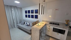 A compact living space with a sofa, dining table, kitchen area, and a set of framed pictures on the wall.