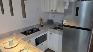A modern kitchen with a stainless steel refrigerator, a gas stove, and a granite countertop. There are hanging pendant lights and a window with blinds.