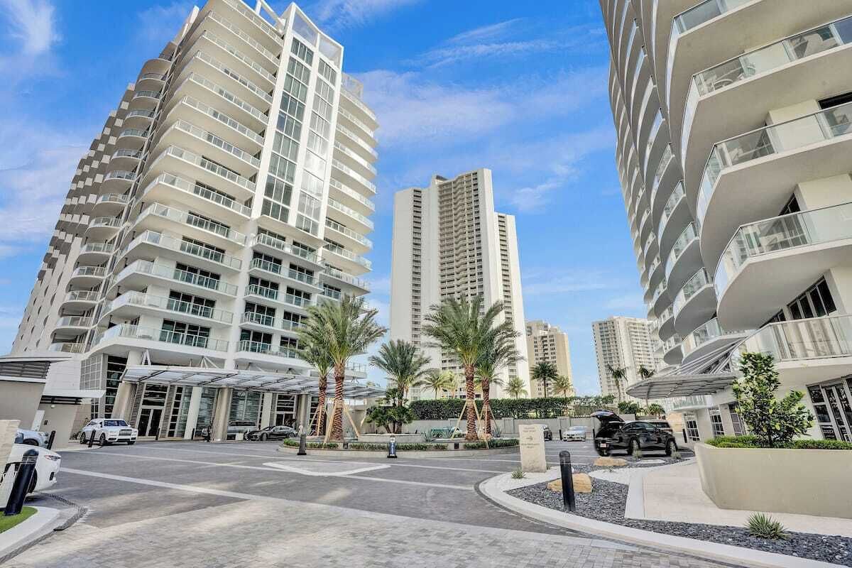 Un hotel moderno de gran altura con varios balcones, una entrada cubierta y palmeras en primer plano.