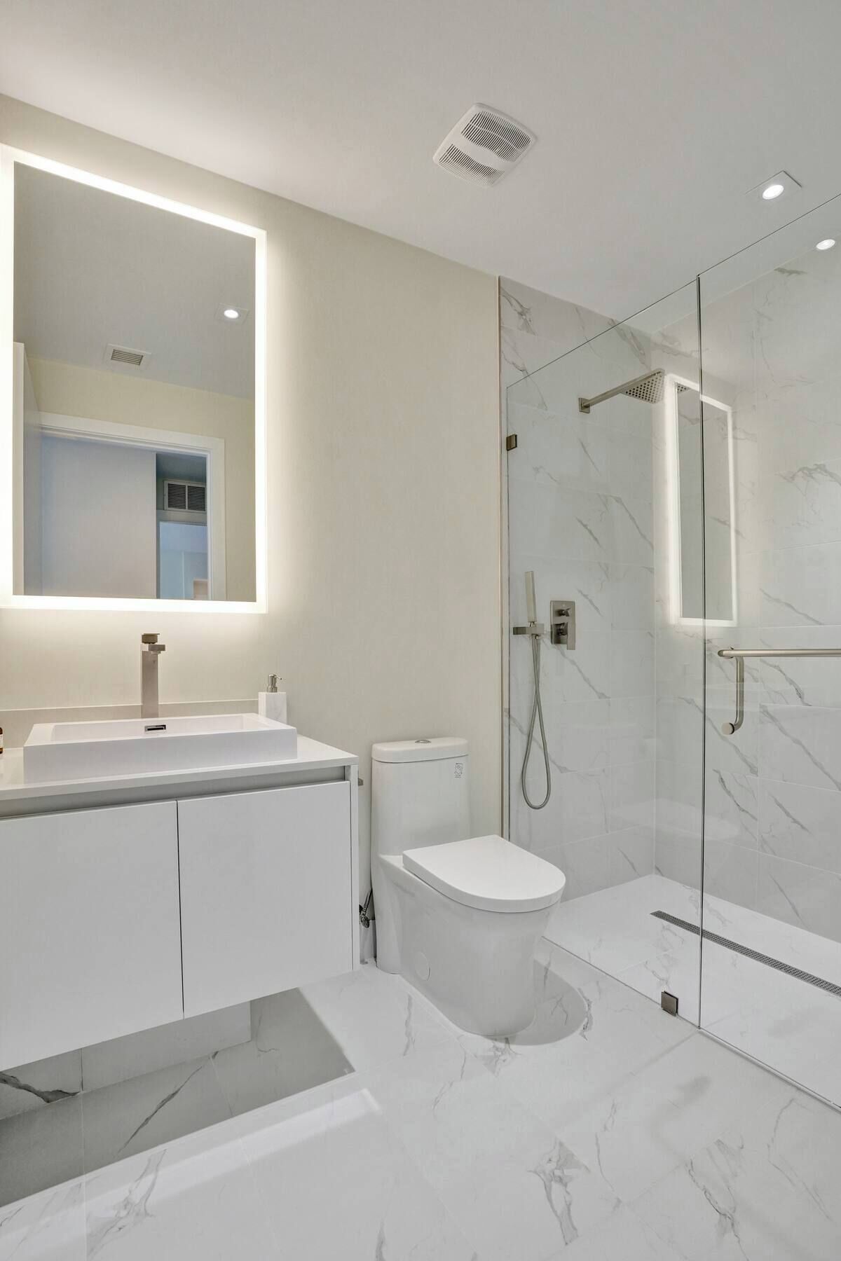 A modern bathroom with a large mirror, a shower enclosure, and a toilet.