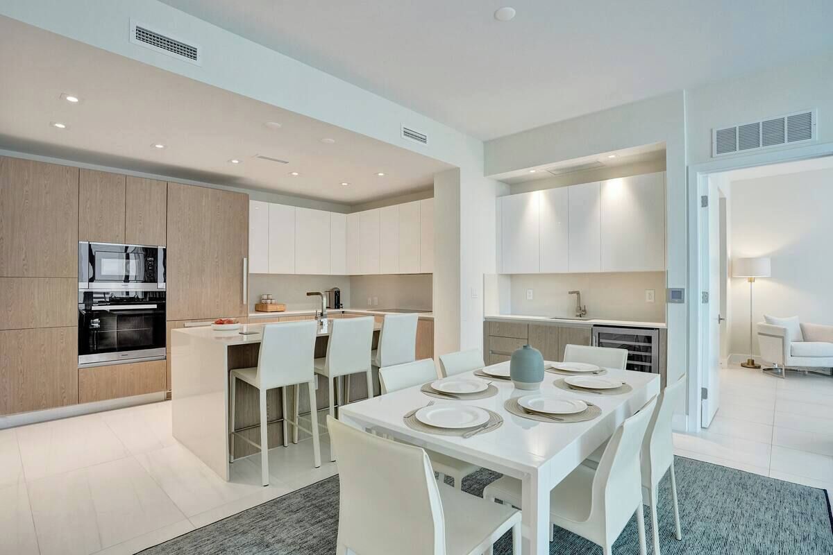 A modern kitchen with white cabinetry, a central island with seating, and a dining area with white chairs and a table set for four.