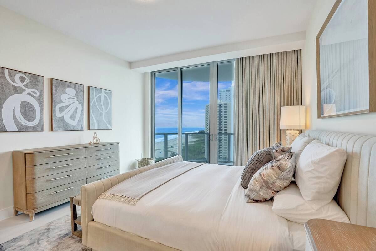 A modern hotel room with a large bed, a dresser, and a view of the city skyline.