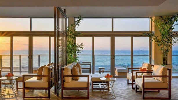 Amplia habitación con grandes ventanales con vistas al mar, amueblada con sofás y una mesita.