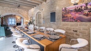 Un espace repas avec une longue table en bois dressée pour un repas, des murs en pierre et une fresque représentant une scène de rue.