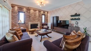 A modern living room with a stone accent wall, a fireplace, a flat-screen TV, and a comfortable seating area. - Iris Villa (Rethymno)