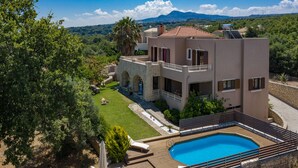 A modern two-story house with a swimming pool, surrounded by lush greenery and mountains in the background.