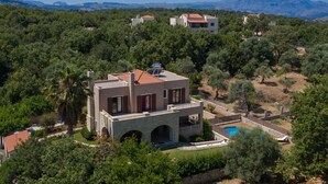 A modern villa with a pool, surrounded by lush greenery and mountains in the background. - Iris Villa (Rethymno)