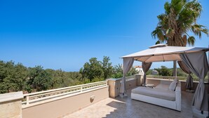 A rooftop terrace with a beige sofa, an umbrella, and a palm tree. - Iris Villa (Rethymno)