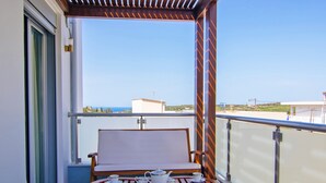 A balcony with a wooden table set for tea, a white cushioned bench, and a clear view of the sea and buildings in the distance. - Bessie's dream Villa (Rethymno)