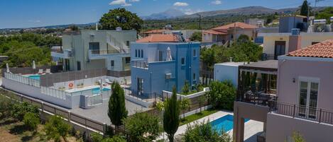 A residential area with modern houses, a swimming pool, and a mountainous backdrop.
